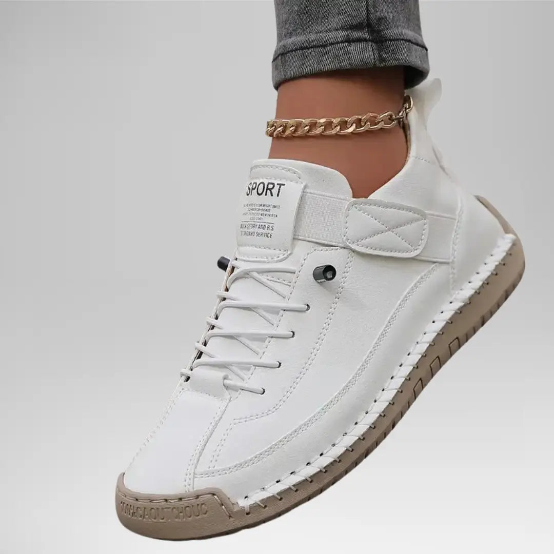 White sneaker with beige sole worn by a person on a light gray background